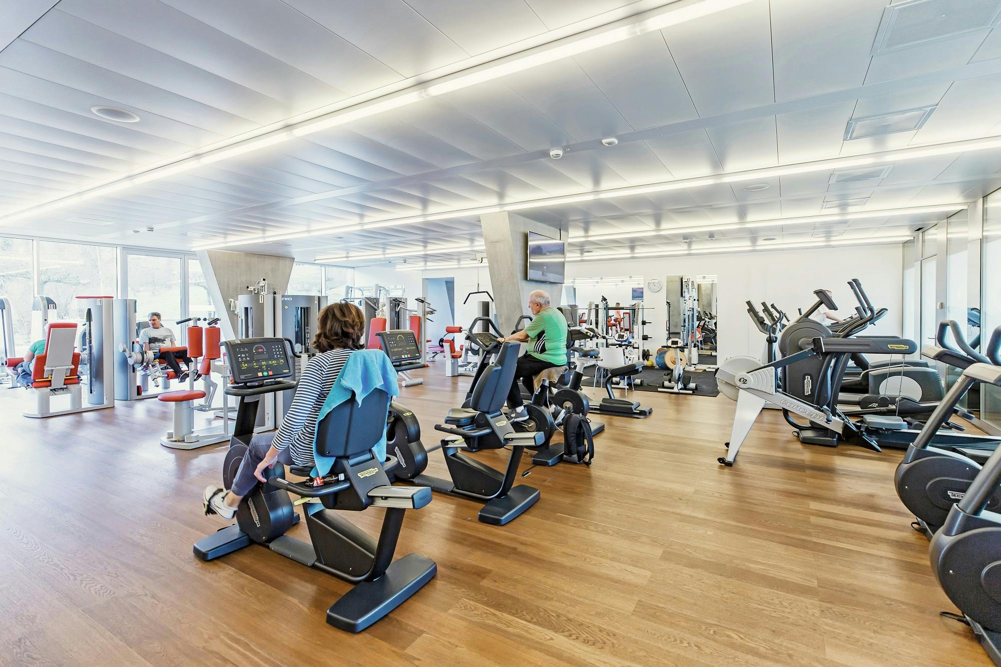 Fitnessstudio mit Personen, die Cardio- und Krafttraining machen.