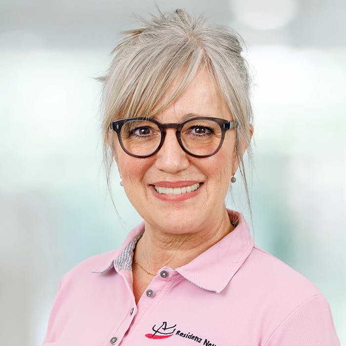 Porträt einer lächelnden älteren Frau mit grauen Haaren und Brille, trägt ein rosa Polohemd.